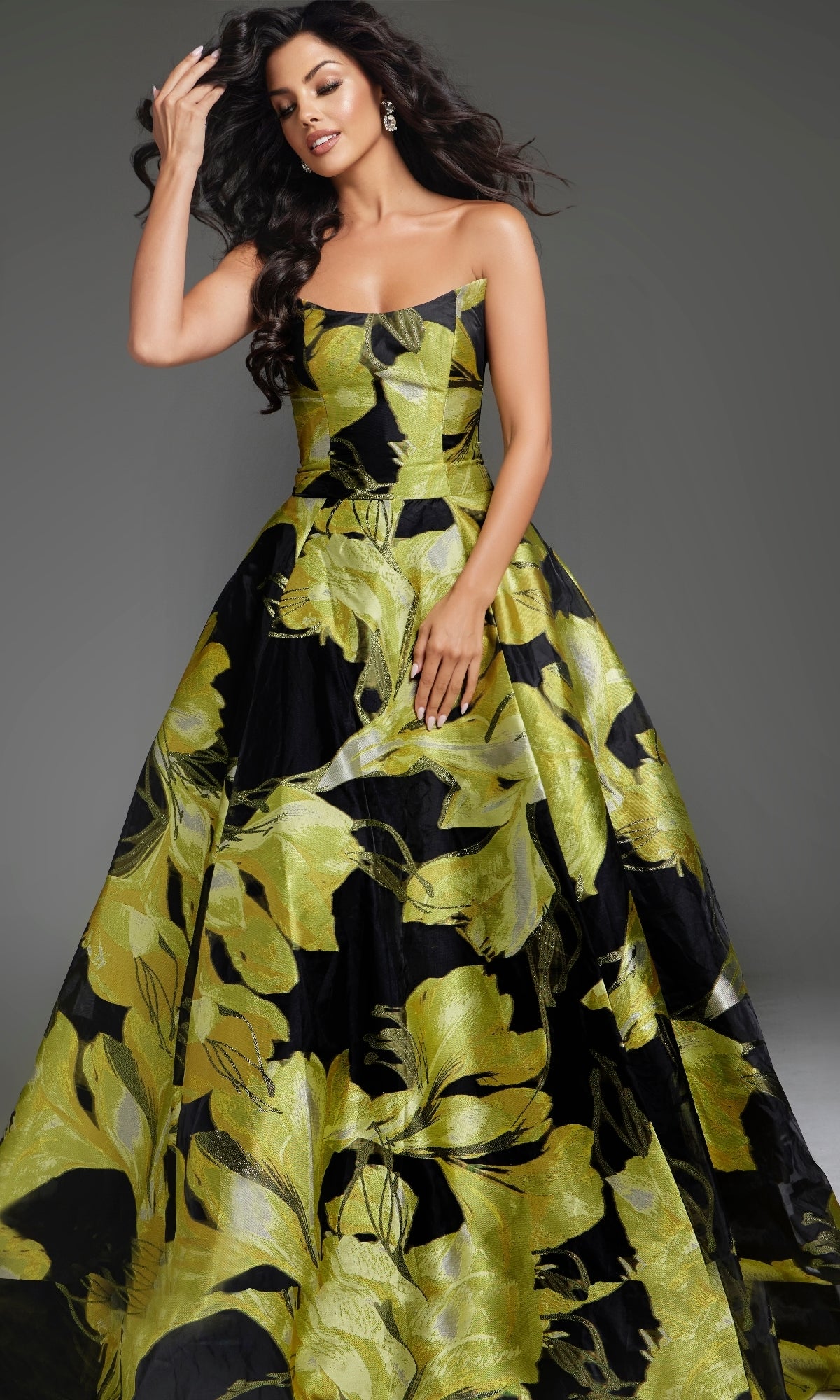 A woman models the Jovani 42435 long prom dress, a strapless gown with a bold green and yellow floral pattern, set against a plain gray background.